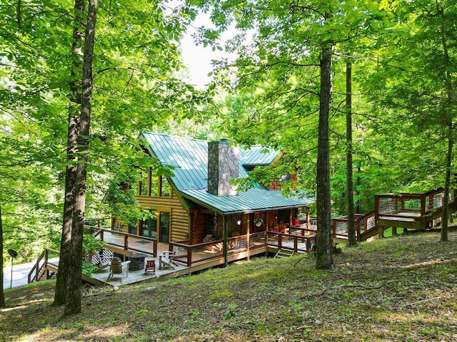 exterior space with a standing seam roof, a chimney, metal roof, log siding, and a wooden deck