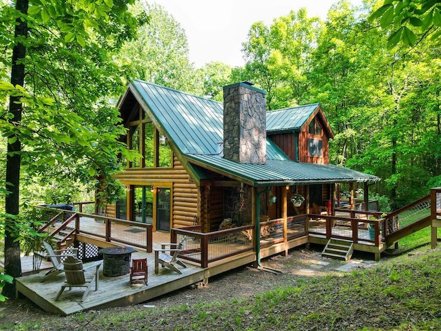 back of property featuring log exterior, a deck, a chimney, a standing seam roof, and metal roof