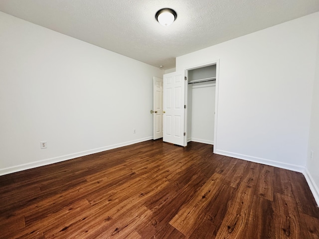 unfurnished bedroom with a textured ceiling, baseboards, dark wood finished floors, and a closet