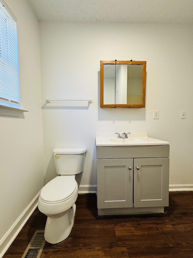 half bath featuring vanity, baseboards, wood finished floors, and visible vents