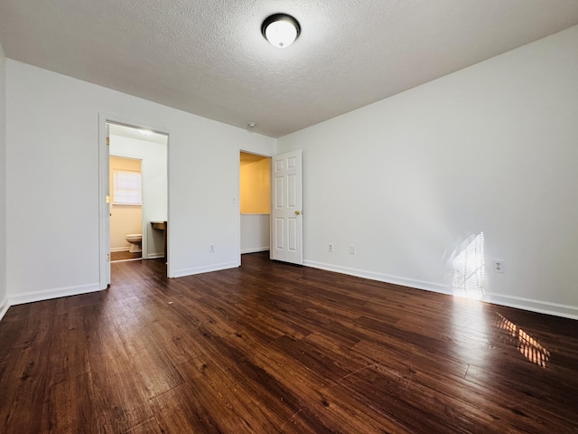 unfurnished bedroom with baseboards, ensuite bath, dark wood finished floors, and a textured ceiling