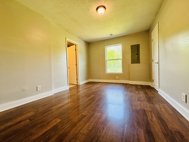 empty room featuring electric panel, a textured ceiling, visible vents, baseboards, and dark wood-type flooring