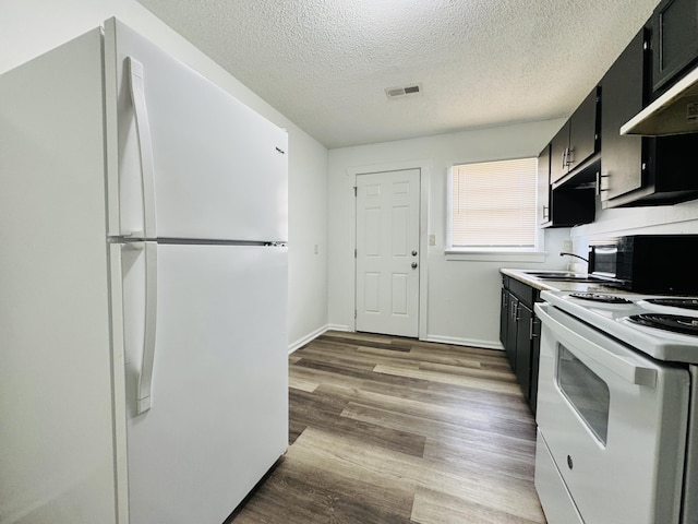 kitchen with white appliances, light wood-type flooring, a textured ceiling, dark cabinets, and a sink