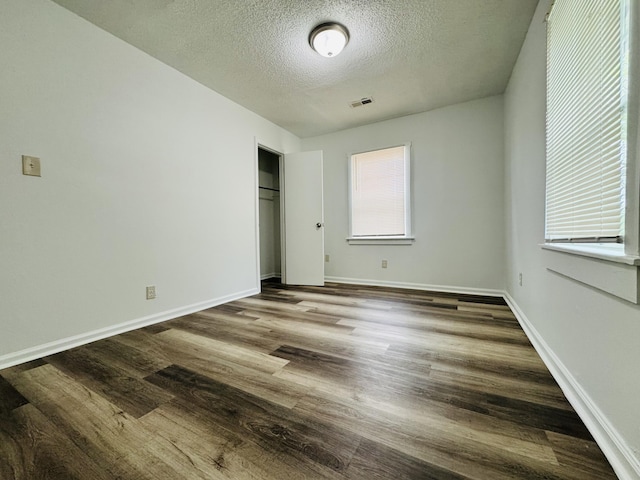 unfurnished bedroom with a textured ceiling, visible vents, dark wood finished floors, baseboards, and a closet