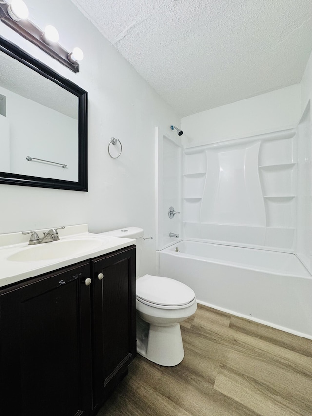 full bath with vanity, wood finished floors, toilet, bathtub / shower combination, and a textured ceiling