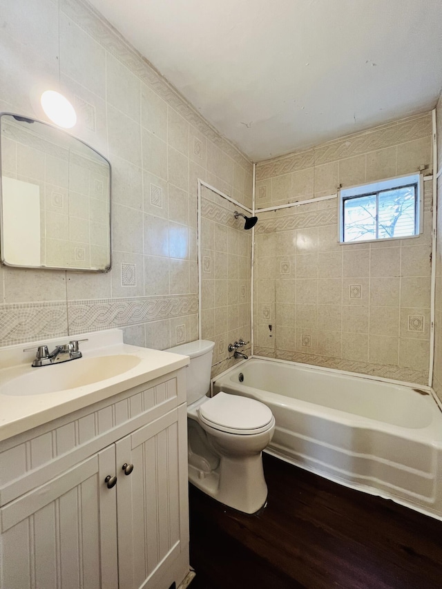 full bathroom with tile walls, wood finished floors, vanity, toilet, and washtub / shower combination
