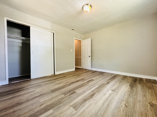 unfurnished bedroom featuring a closet, baseboards, wood finished floors, and visible vents