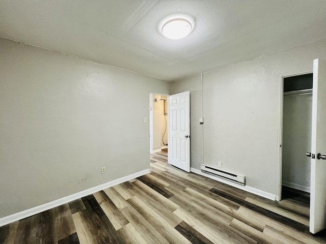 unfurnished bedroom featuring baseboards, baseboard heating, a closet, and wood finished floors