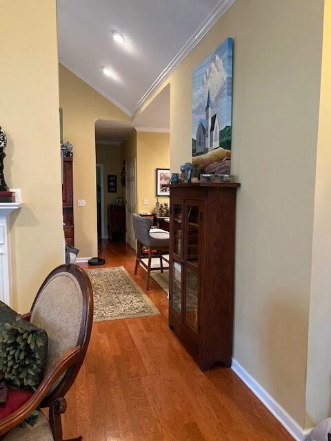 corridor featuring crown molding, wood finished floors, lofted ceiling, and baseboards