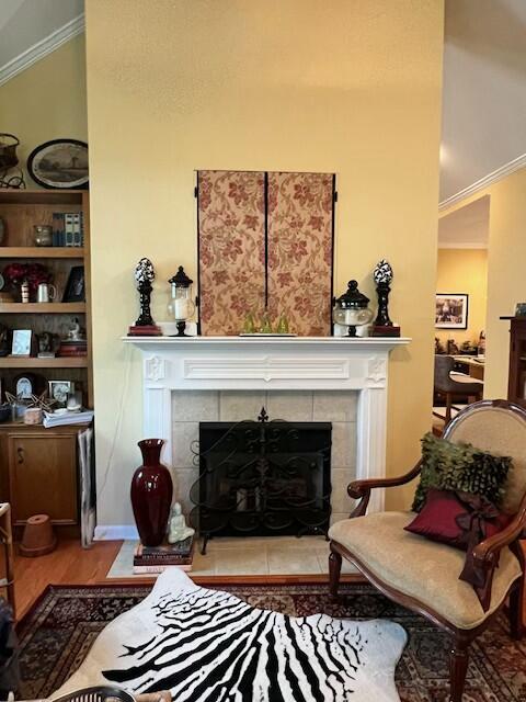 sitting room with a tile fireplace, wood finished floors, ornamental molding, and built in shelves