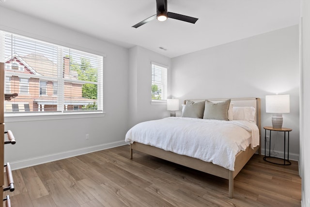 bedroom with a ceiling fan, visible vents, wood finished floors, and baseboards