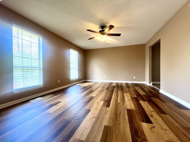 spare room featuring a ceiling fan, dark wood-style flooring, visible vents, and baseboards