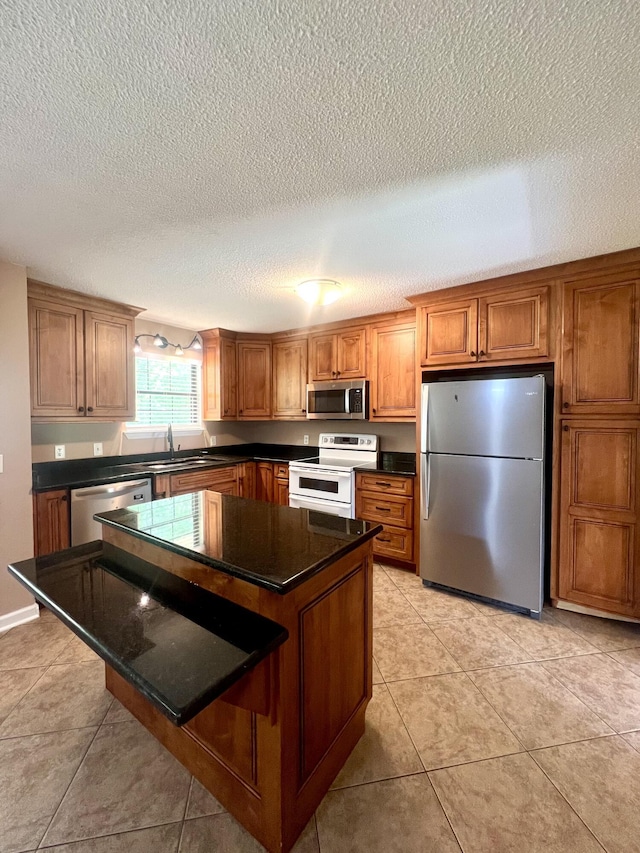 kitchen featuring a textured ceiling, brown cabinets, a sink, appliances with stainless steel finishes, and dark countertops