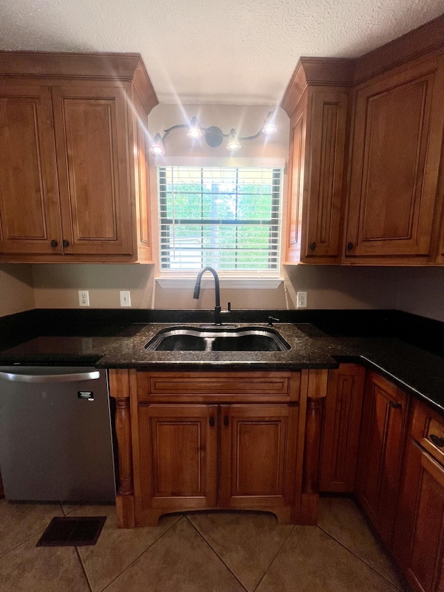 kitchen with stainless steel dishwasher, light tile patterned flooring, a sink, and brown cabinetry