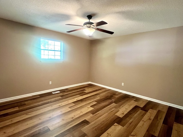 spare room with dark wood-style flooring, a ceiling fan, visible vents, baseboards, and a textured ceiling