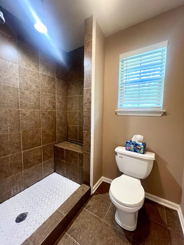 bathroom with toilet, a tile shower, tile patterned floors, and baseboards
