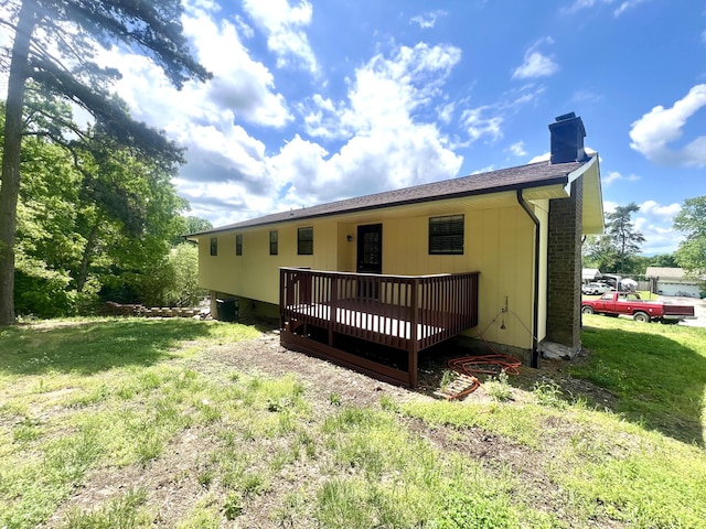 back of house with a chimney, a wooden deck, and a lawn