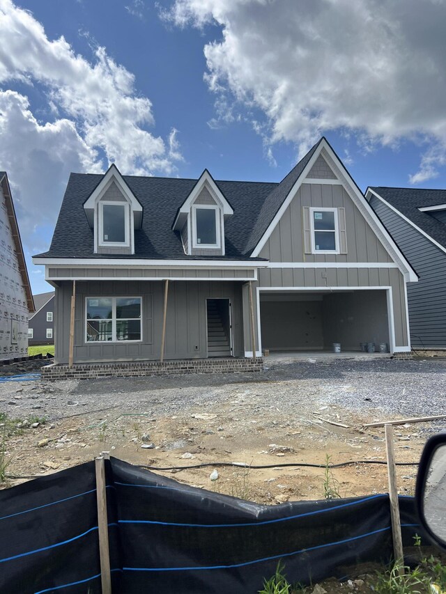 view of front of house with driveway, roof with shingles, board and batten siding, and fence