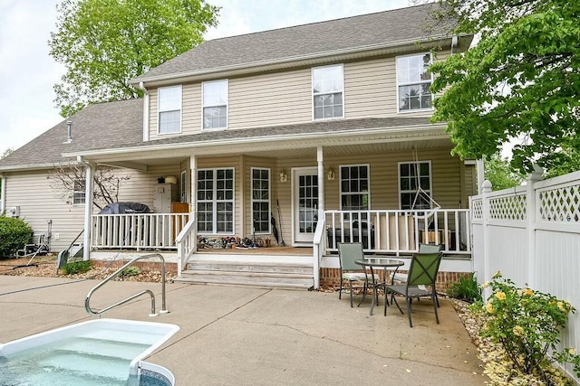 rear view of property featuring a porch, roof with shingles, and fence