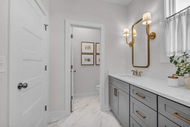 bathroom with toilet, vanity, marble finish floor, and baseboards
