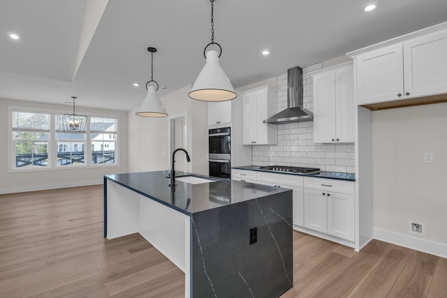 kitchen with dark countertops, a sink, appliances with stainless steel finishes, and wall chimney range hood