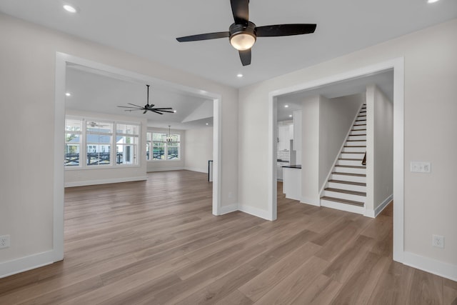 unfurnished living room with light wood-type flooring, ceiling fan with notable chandelier, stairs, and recessed lighting