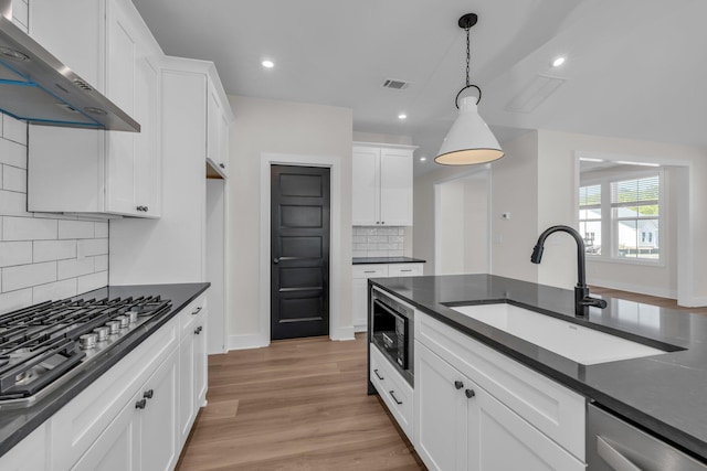 kitchen featuring stainless steel appliances, dark countertops, a sink, visible vents, and wall chimney exhaust hood