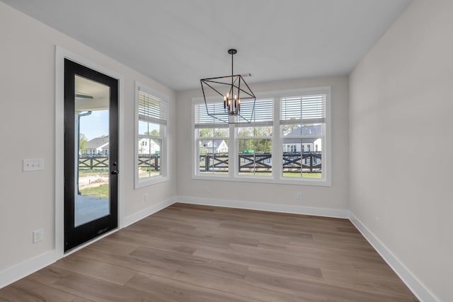 unfurnished dining area with an inviting chandelier, wood finished floors, and baseboards