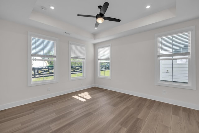empty room featuring a tray ceiling, baseboards, recessed lighting, wood finished floors, and a ceiling fan