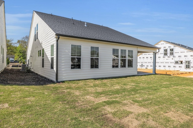 back of property featuring a shingled roof, cooling unit, and a yard