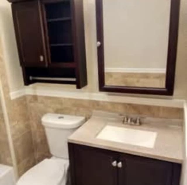 bathroom with vanity, a wainscoted wall, toilet, and tile walls