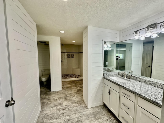 bathroom with a textured ceiling, wood finished floors, vanity, and a stall shower
