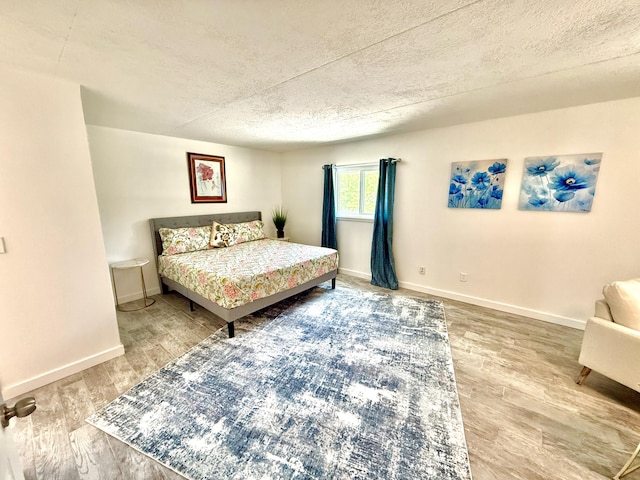 bedroom with a textured ceiling, wood finished floors, and baseboards