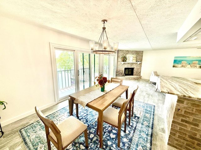 dining room featuring a brick fireplace, a textured ceiling, a notable chandelier, and wood finished floors