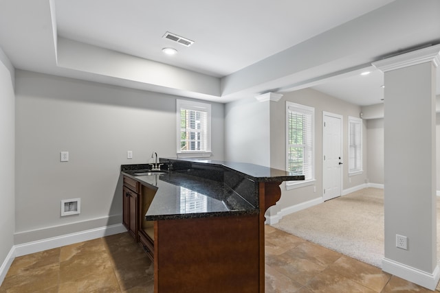 kitchen with visible vents, a peninsula, a kitchen bar, dark stone counters, and a sink