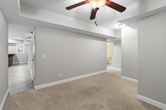 below grade area featuring baseboards, ceiling fan, and light colored carpet