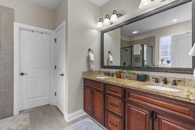 bathroom with a sink, baseboards, a shower stall, and double vanity