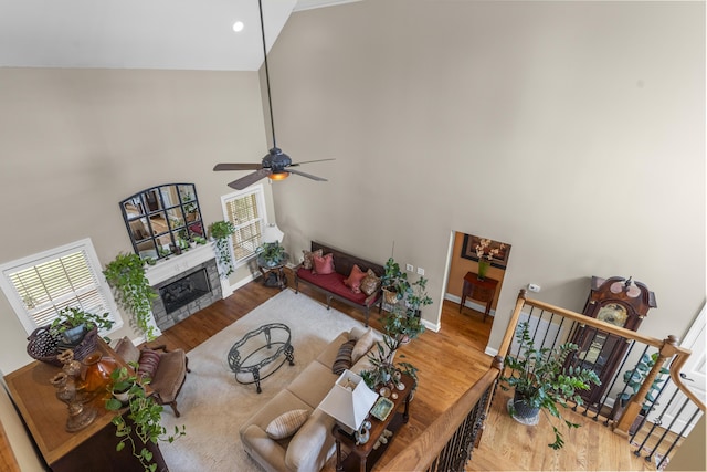 living area featuring ceiling fan, wood finished floors, high vaulted ceiling, baseboards, and a glass covered fireplace