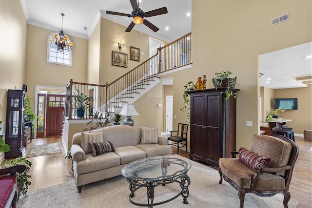 living area with light wood-style flooring, a towering ceiling, visible vents, ornamental molding, and stairway