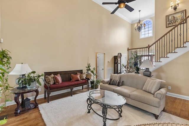living area featuring crown molding, a high ceiling, ceiling fan with notable chandelier, baseboards, and wood finished floors