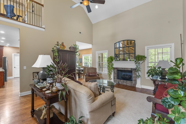 living area with high vaulted ceiling, ceiling fan, a fireplace, and wood finished floors
