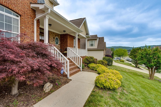 entrance to property featuring a porch, brick siding, a mountain view, a yard, and a shingled roof