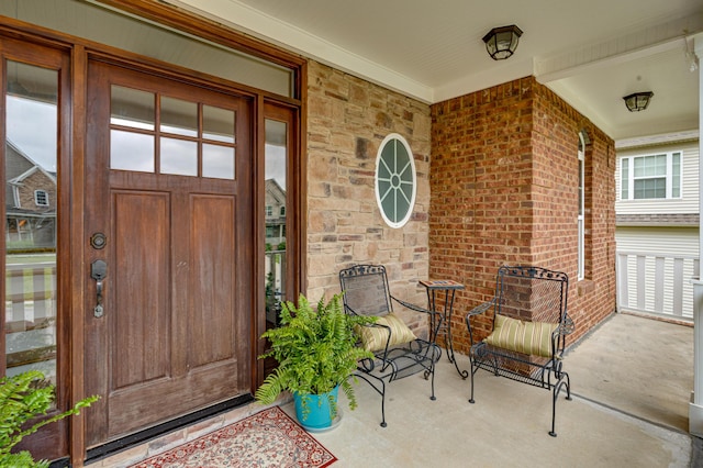 view of exterior entry featuring brick siding, covered porch, and stone siding