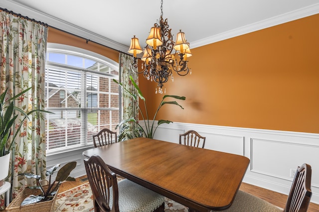 dining area with crown molding, wainscoting, wood finished floors, a chandelier, and a decorative wall