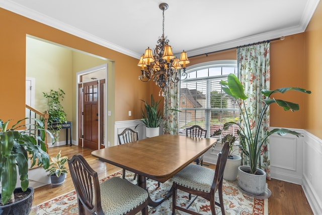 dining room with crown molding, a notable chandelier, wainscoting, and wood finished floors