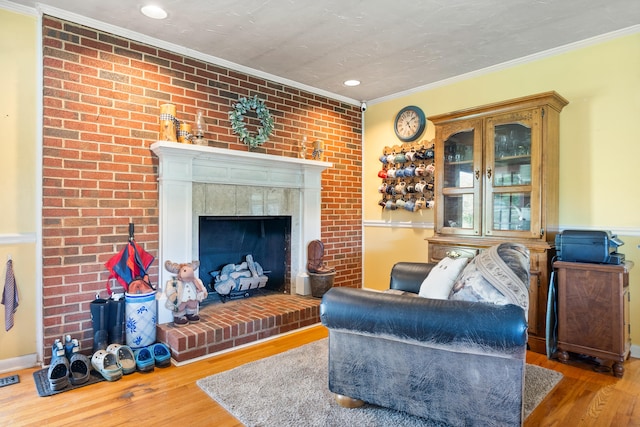 living area with crown molding, a brick fireplace, recessed lighting, and wood finished floors