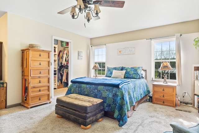 carpeted bedroom featuring a closet, a ceiling fan, and a walk in closet