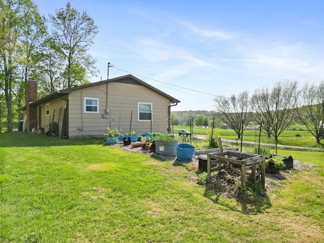 rear view of house with a chimney, a yard, and a vegetable garden