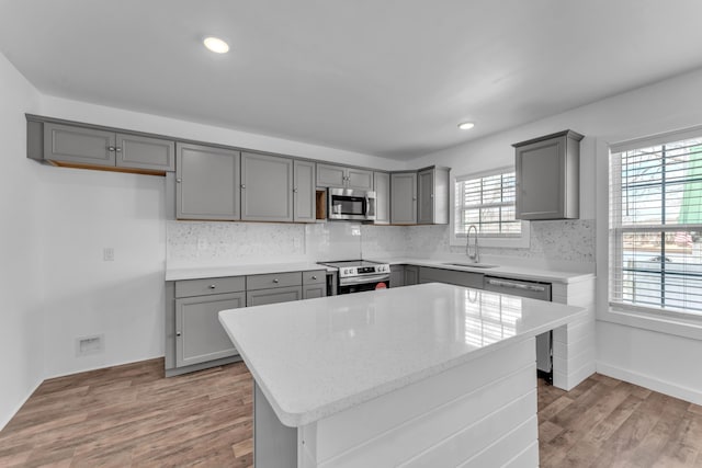 kitchen featuring gray cabinets, decorative backsplash, appliances with stainless steel finishes, light wood-type flooring, and a sink