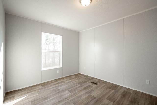 spare room with wood finished floors, visible vents, and baseboards